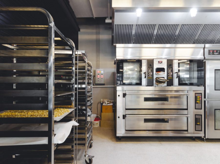 Modern pastry kitchen decorated in black, white and steel with baking machine, oven, conveyor, production line, mixer and cooling plant.